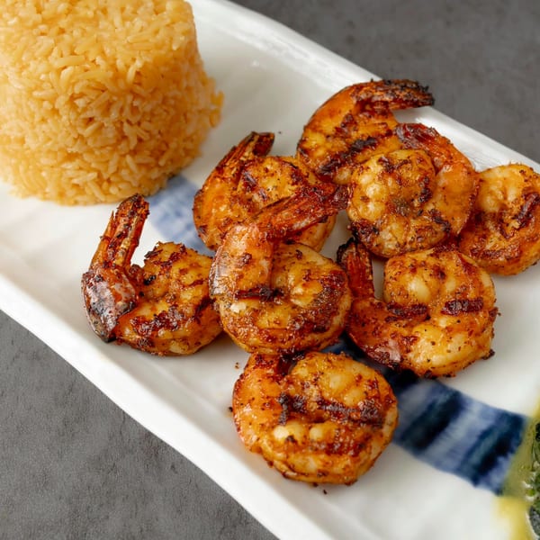 Grilled shrimp and a mound of yellow rice on a white rectangular plate with blue accents.
