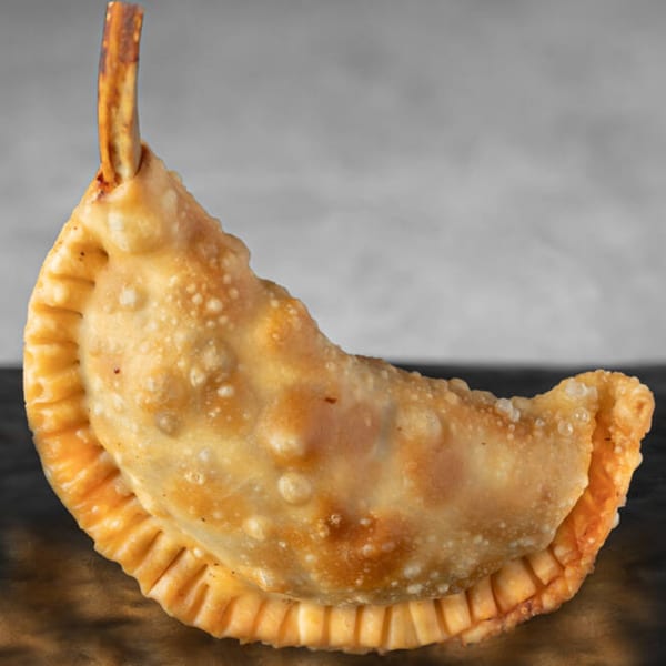 A golden-brown, crescent-shaped Supreme Empanada with a crispy, crimped edge and a small stick.